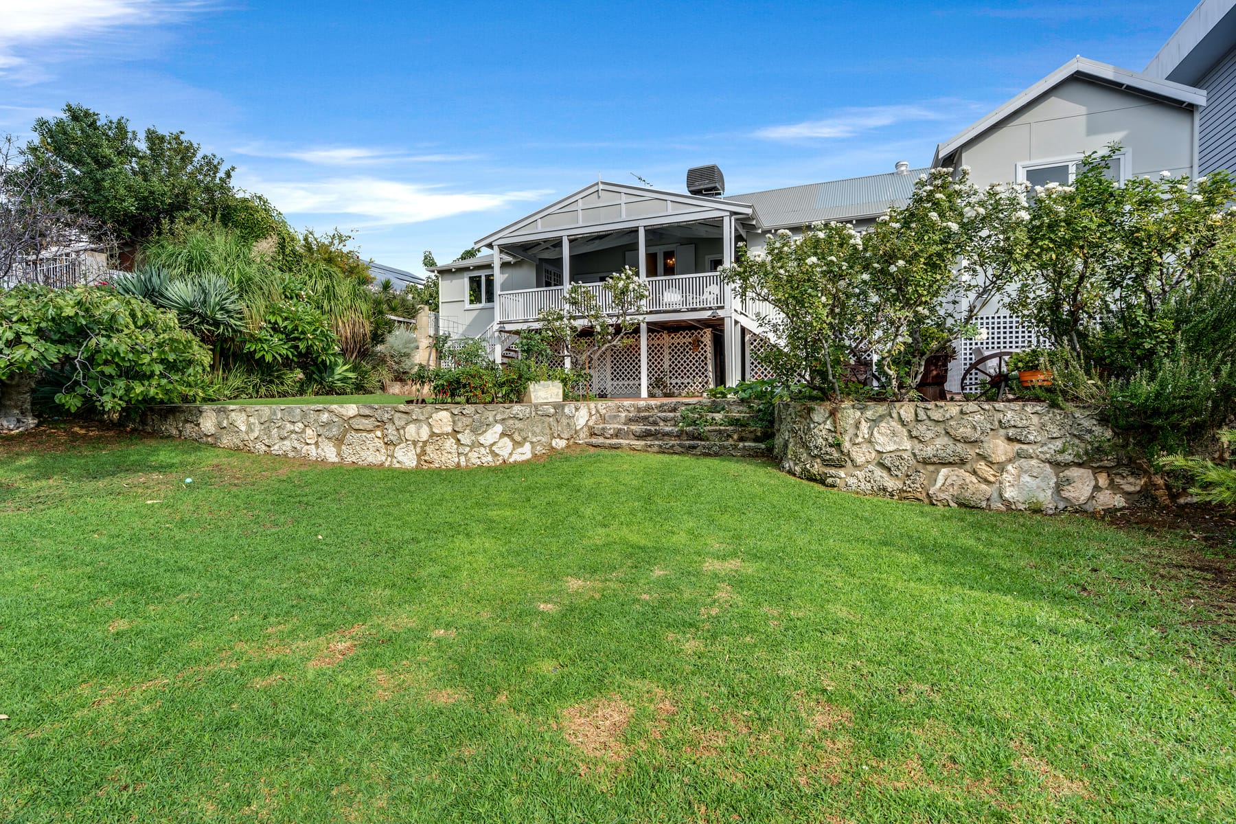 Rear garden with lawn, stone wall and elevated home